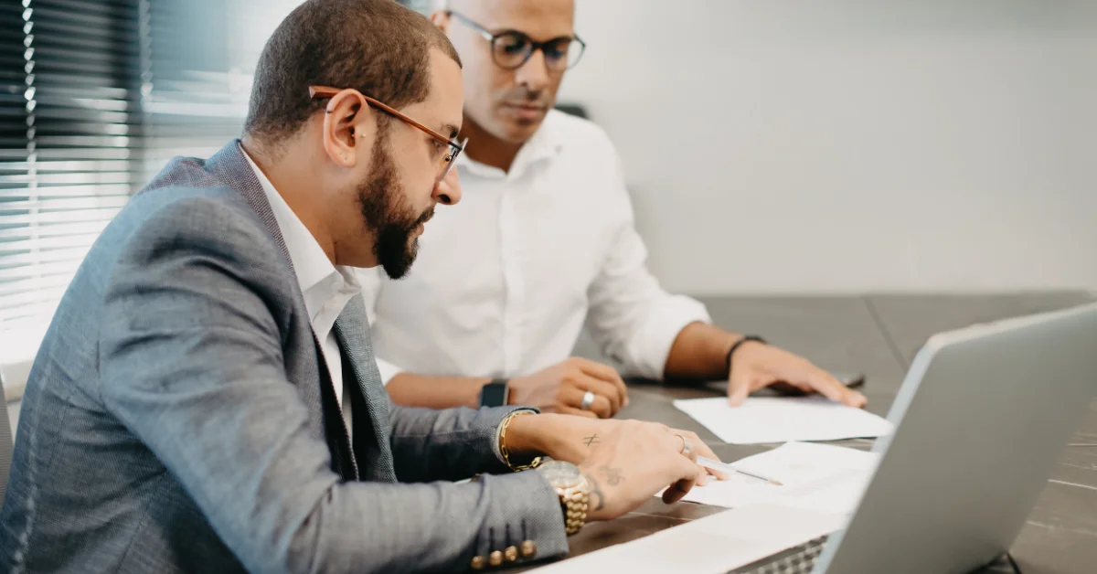two businessmen sitting at desk discussing reports on paper